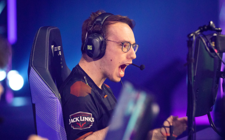 A bespectacled Valorant player sits in front of the monitor, wearing headphones with a mic and enjoying the play