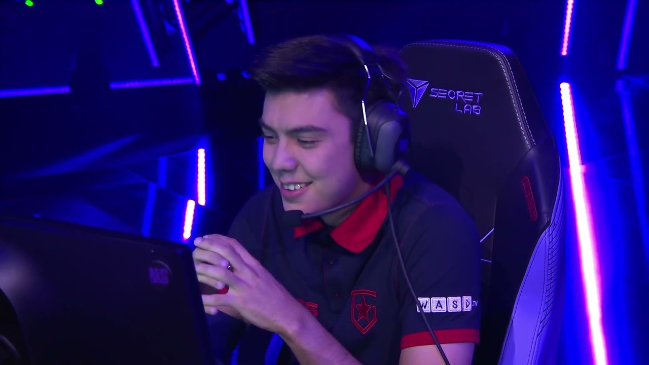 Gentleman is enjoying the game and He is sitting on a chair He has mic headphones in his ears and a monitor in front of him And his hands are clasped together